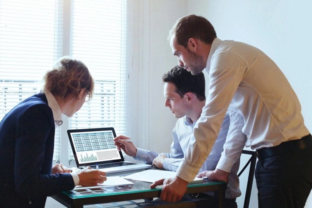 Two men and one woman reviewing information on a desktop computer.