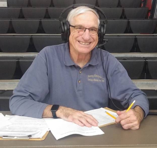 An elderly man with glasses and headphones smiling while writing notes.