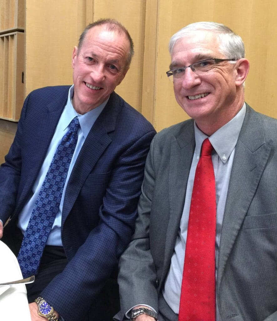 Two men in suits smiling for a photo indoors.