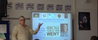 Man presenting a radio station advertisement slide.